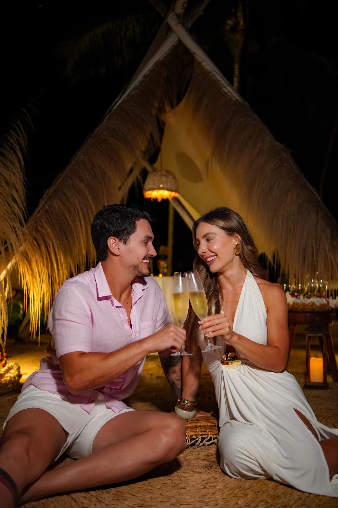 Casal brindando em uma cabana iluminada à noite no Taboo