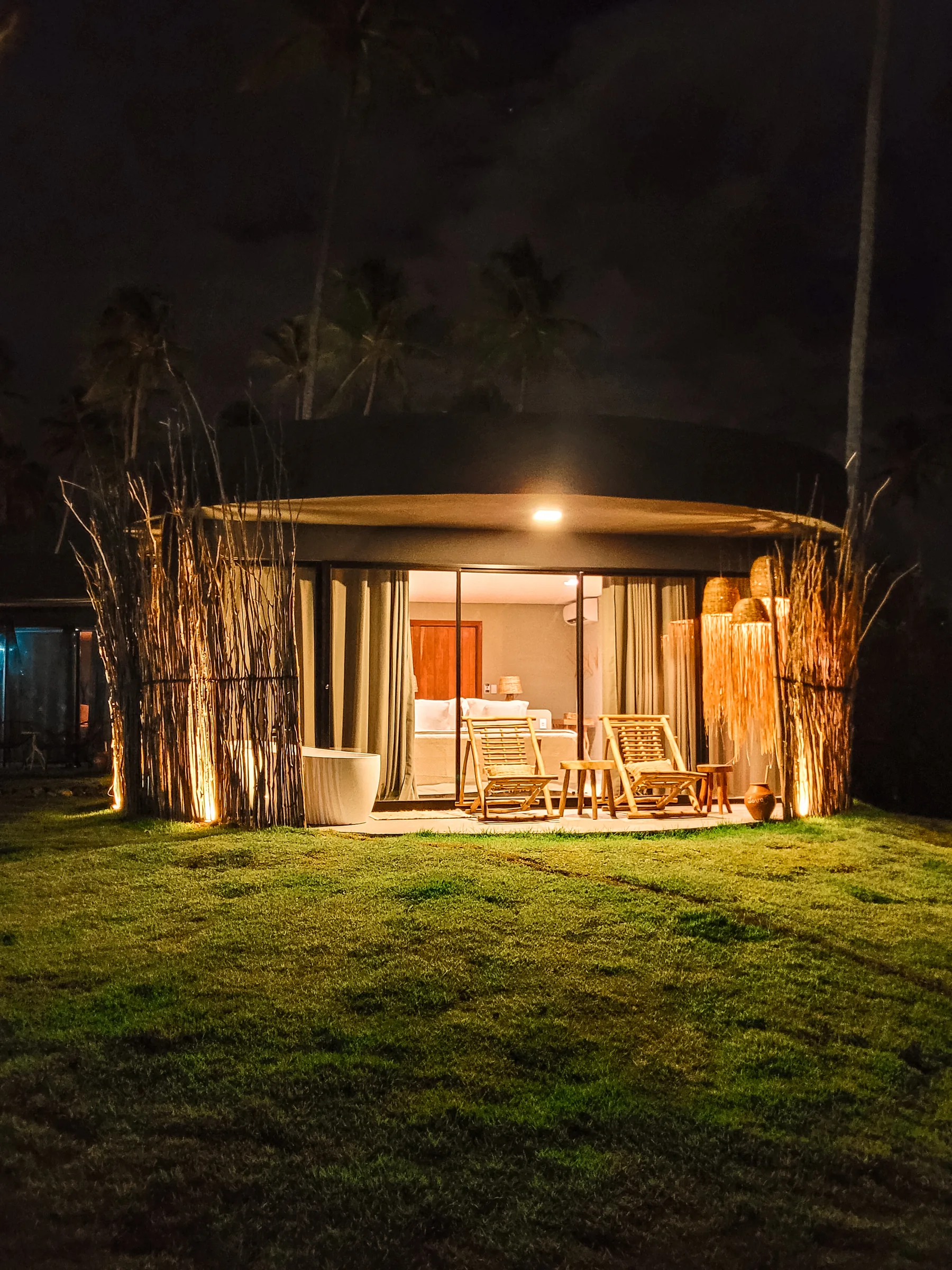 Bangalô do Taboo iluminado à noite, cercado pelo jardim